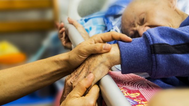 Pacjent hospicjum w łóżku trzyma rodzinę za rękę